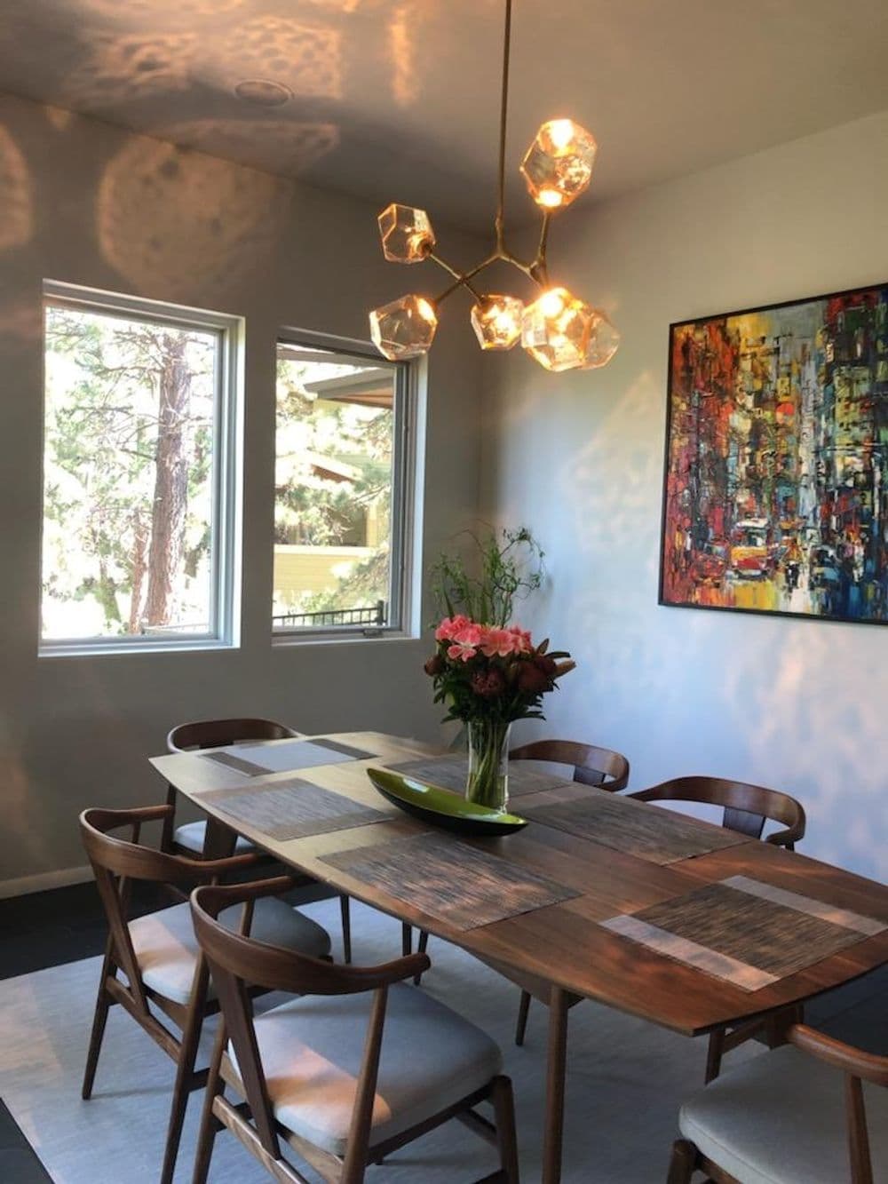 Modern dining room with wooden table, stylish chairs, floral centerpiece, and contemporary art.