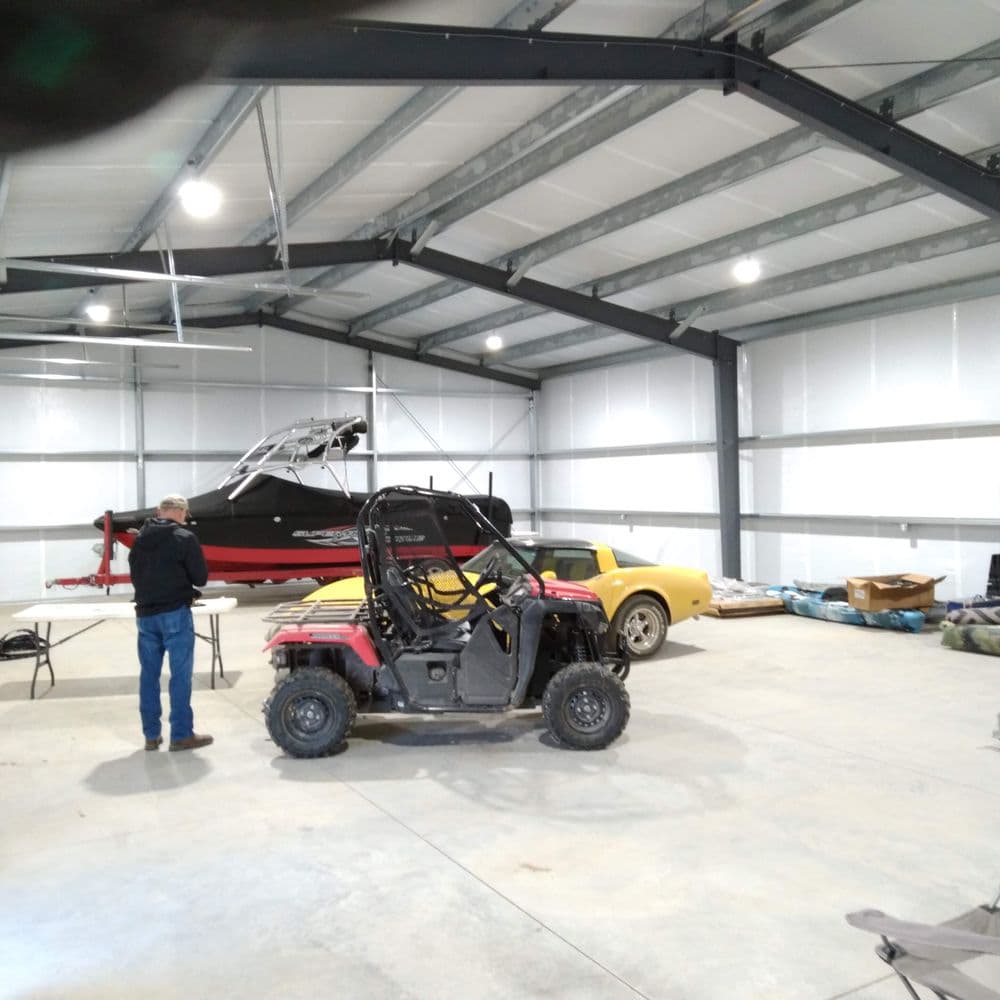 Indoor garage showcasing an ATV, classic car, and a boat in a spacious metal building.