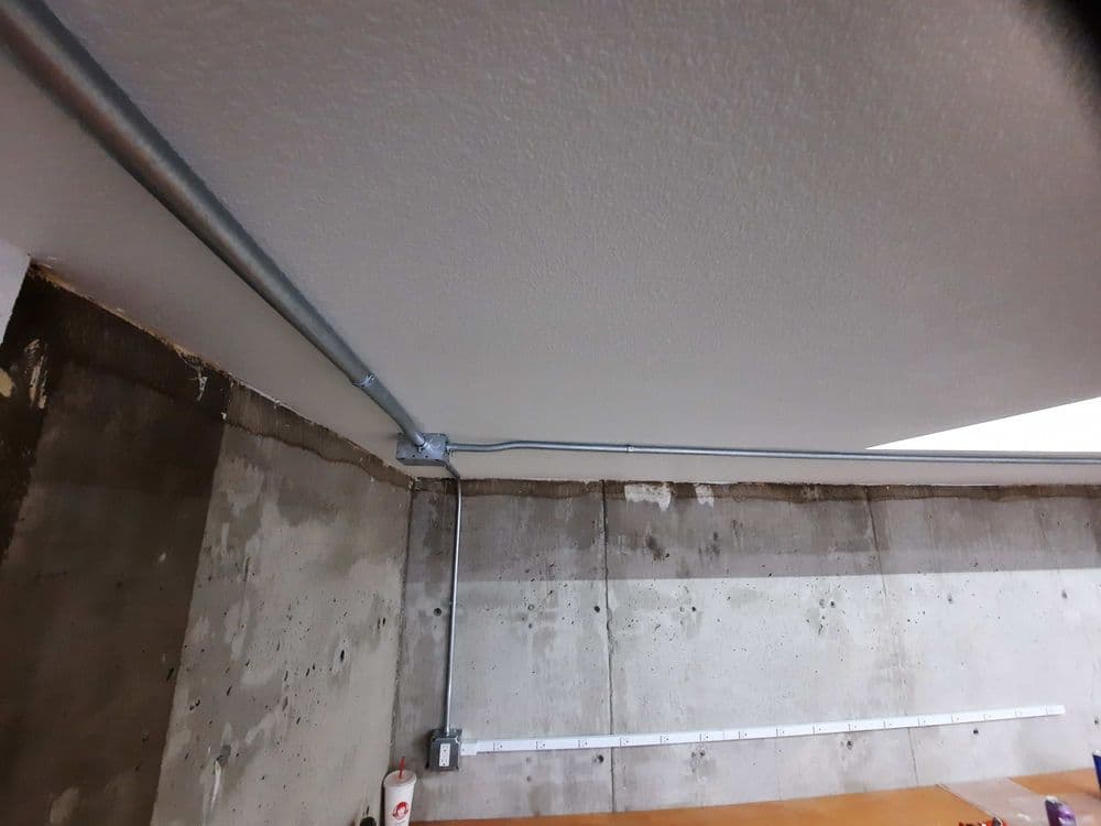 View of a basement ceiling with electrical conduit and walls featuring concrete texture.