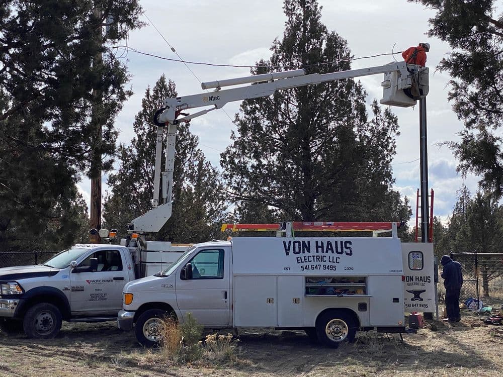 Electrician working on power lines using a cherry picker truck in a forested area.