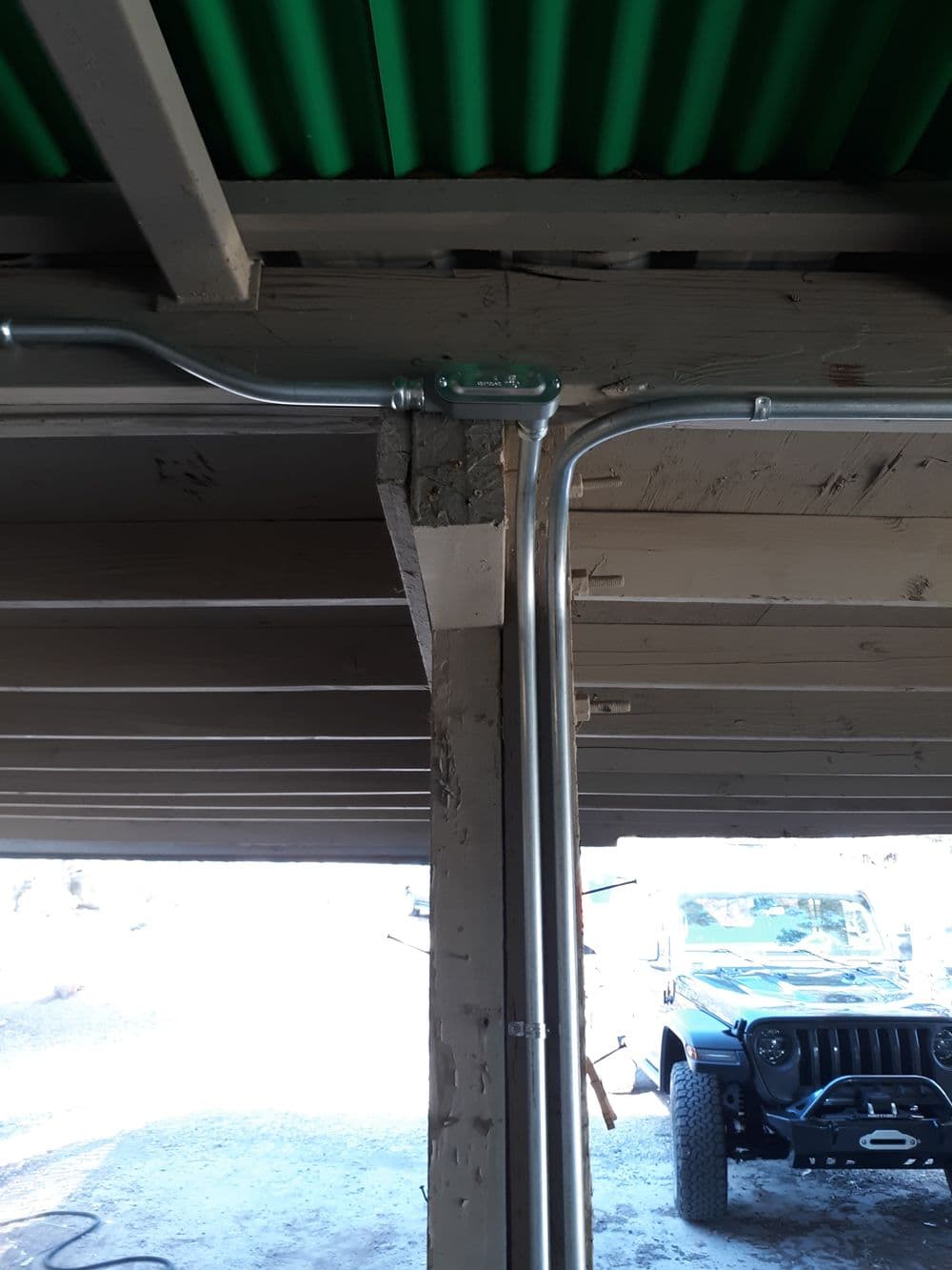 Metal conduit installation on wooden support beam in a garage with visible vehicle.