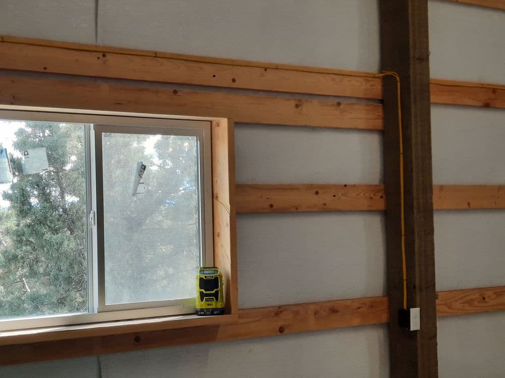Interior view of a wooden wall with a window and a tool on the sill in a construction space.
