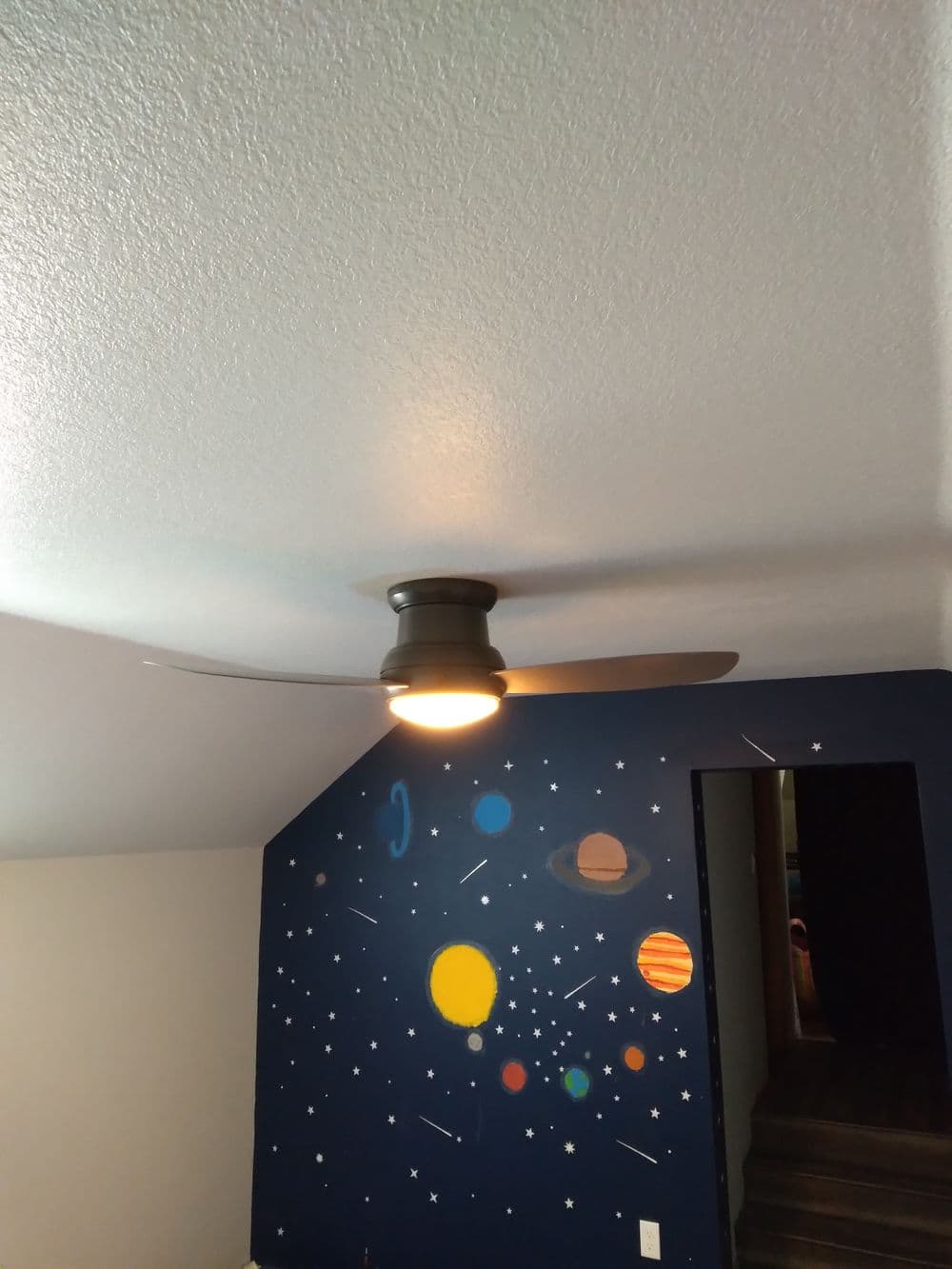 Ceiling fan in a room with a space-themed mural featuring planets and stars.