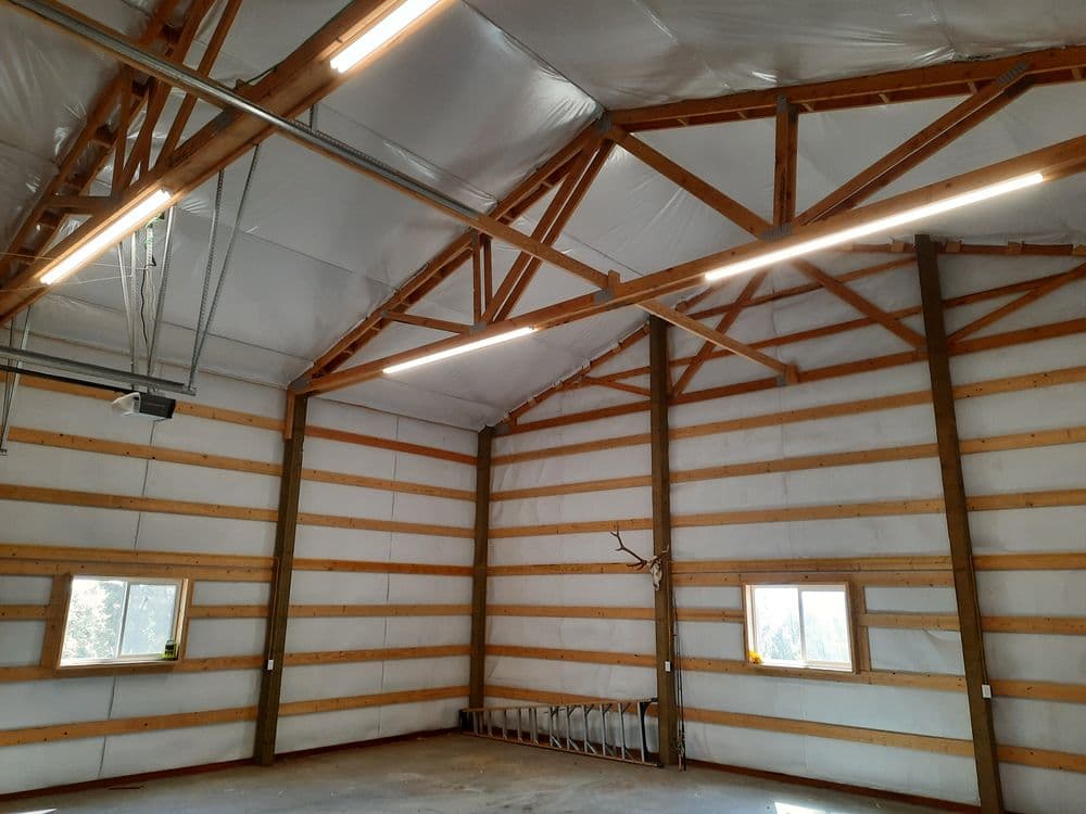 Interior of a spacious building with wooden beams, bright lighting, and windows.