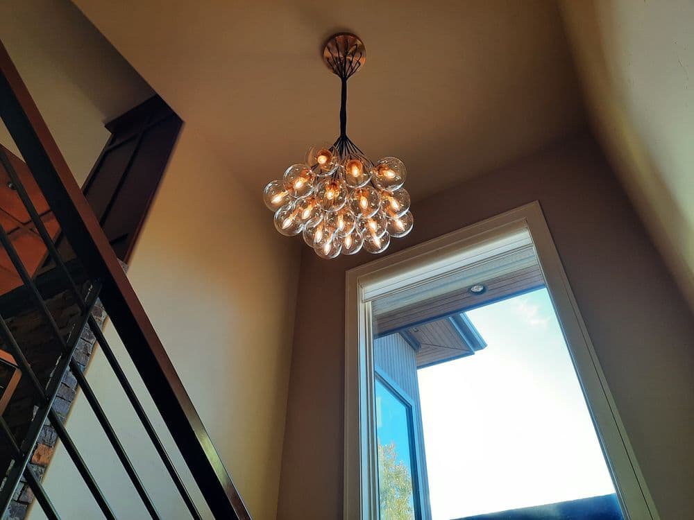 Modern chandelier with multiple glass bulbs hanging from a ceiling above a staircase.