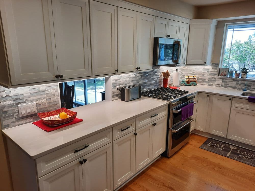 Modern kitchen with white cabinets, sleek countertop, stainless steel appliances, and natural light.