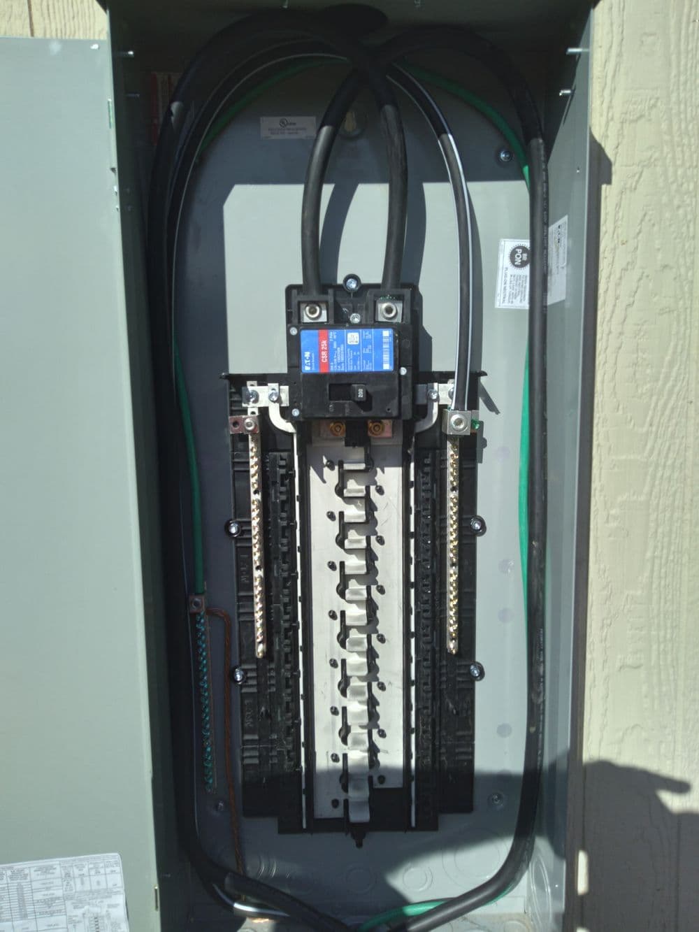 Electrical panel with circuit breakers and wiring, mounted on a wall.
