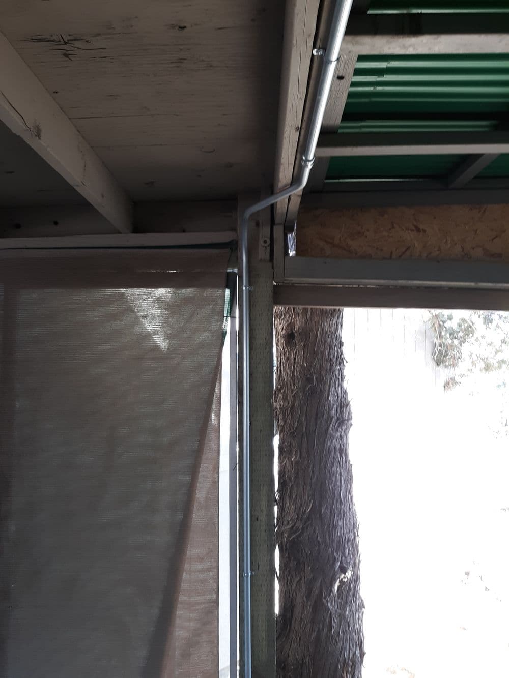 Metal conduit installation at shelter corner with partially drawn outdoor shades.