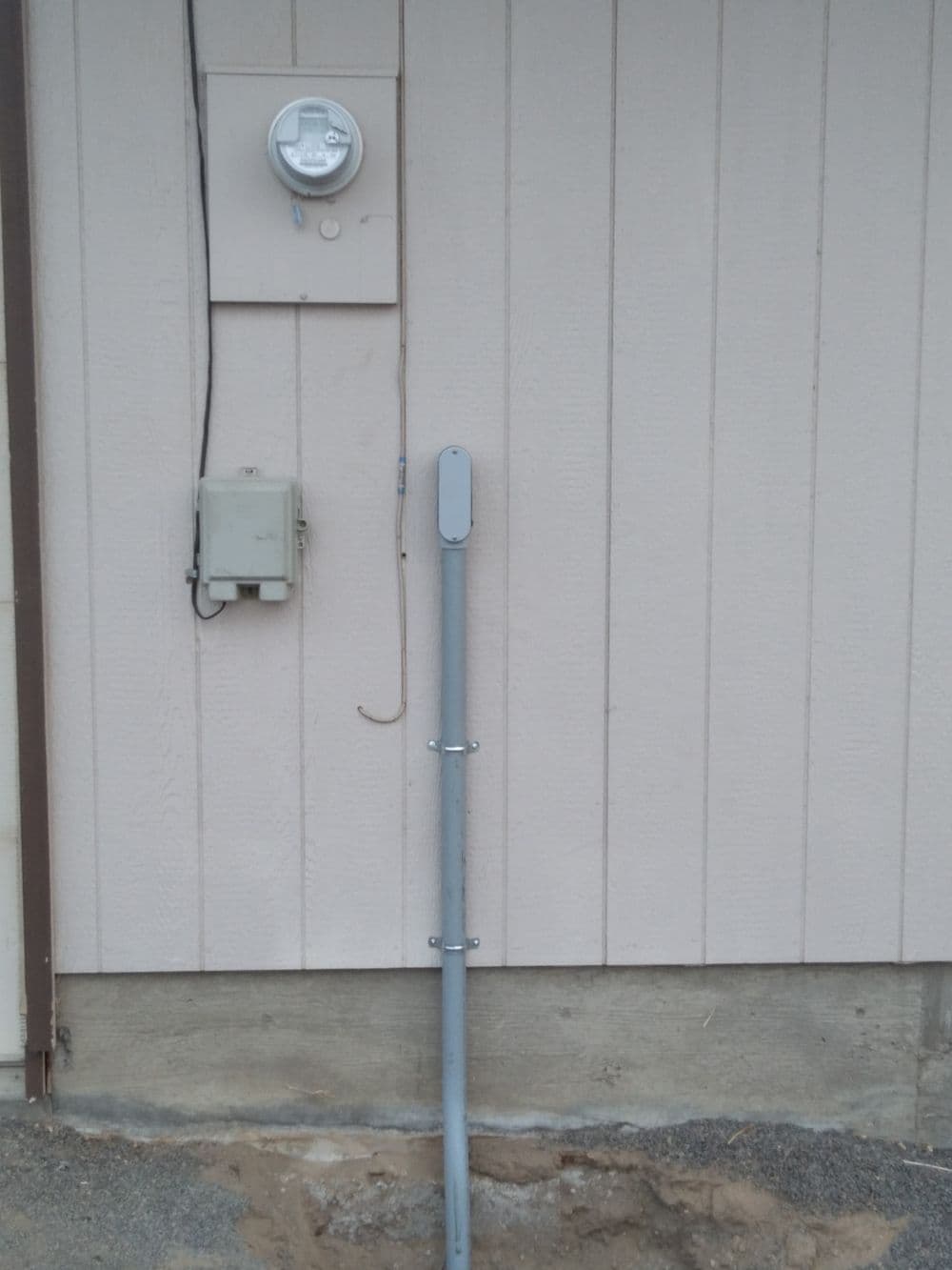 Electric meter and service equipment mounted on a beige wooden wall with a gray conduit.