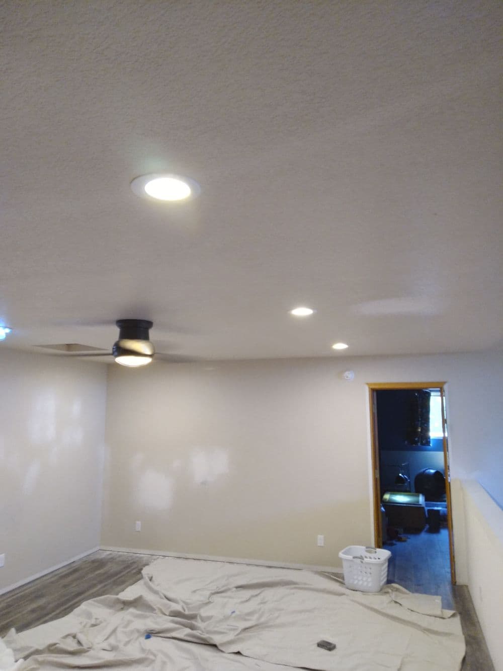 Living room with newly painted walls, recessed lighting, and ceiling fan, featuring a drop cloth on the floor.