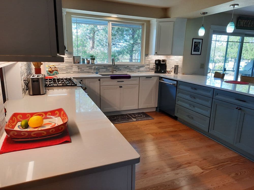 Modern kitchen with hardwood floors, white cabinets, and a bright window view.