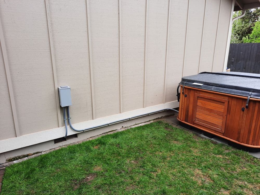 Hot tub installation beside a house with electrical panel and grass.