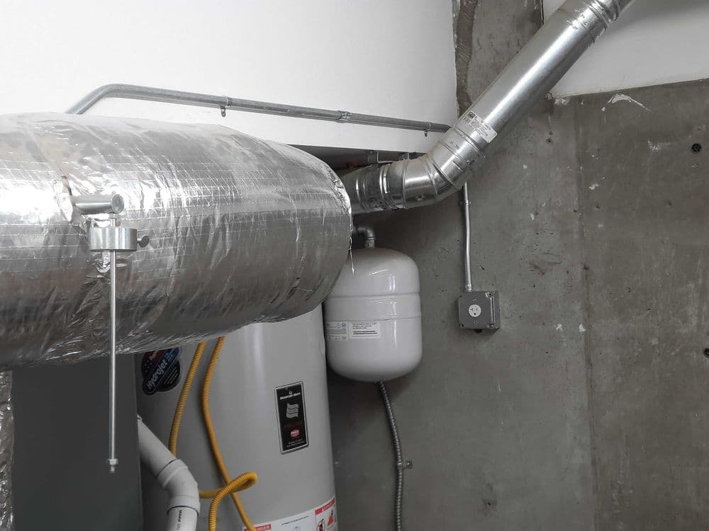 HVAC ductwork and water heater installation in a concrete basement.