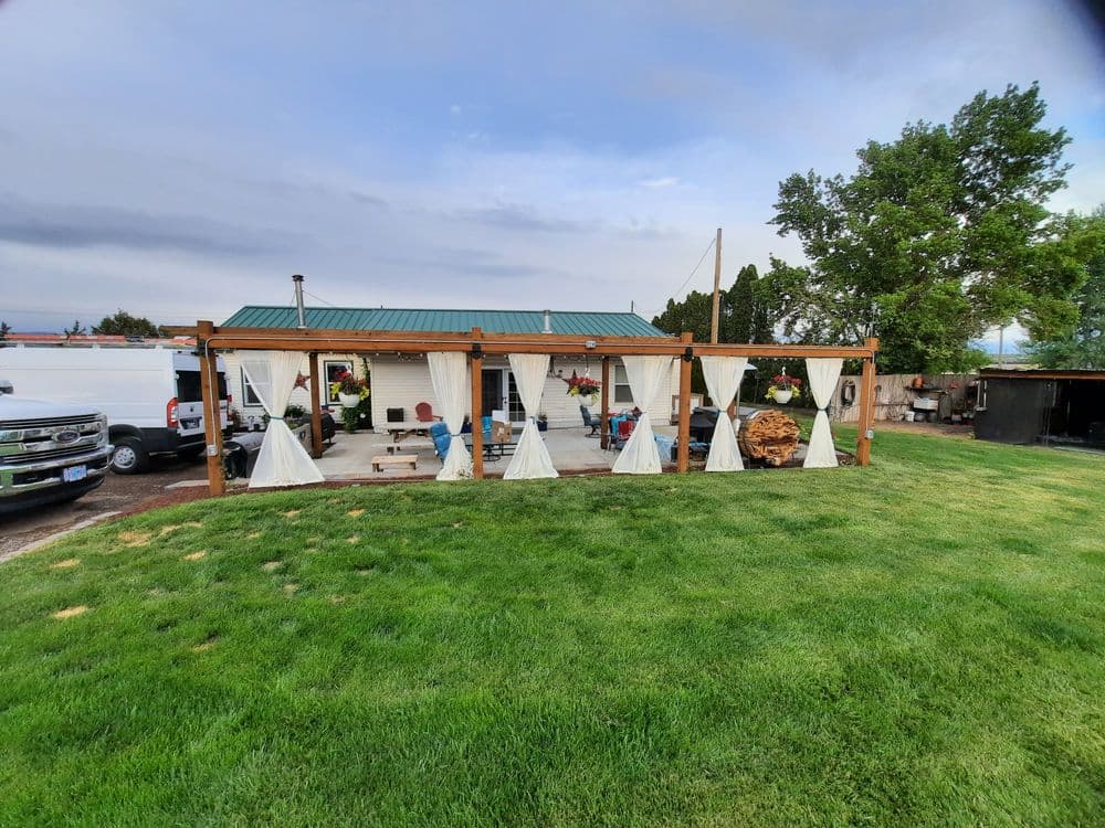 Cozy outdoor patio with curtains, greenery, and seating in a serene landscape setting.