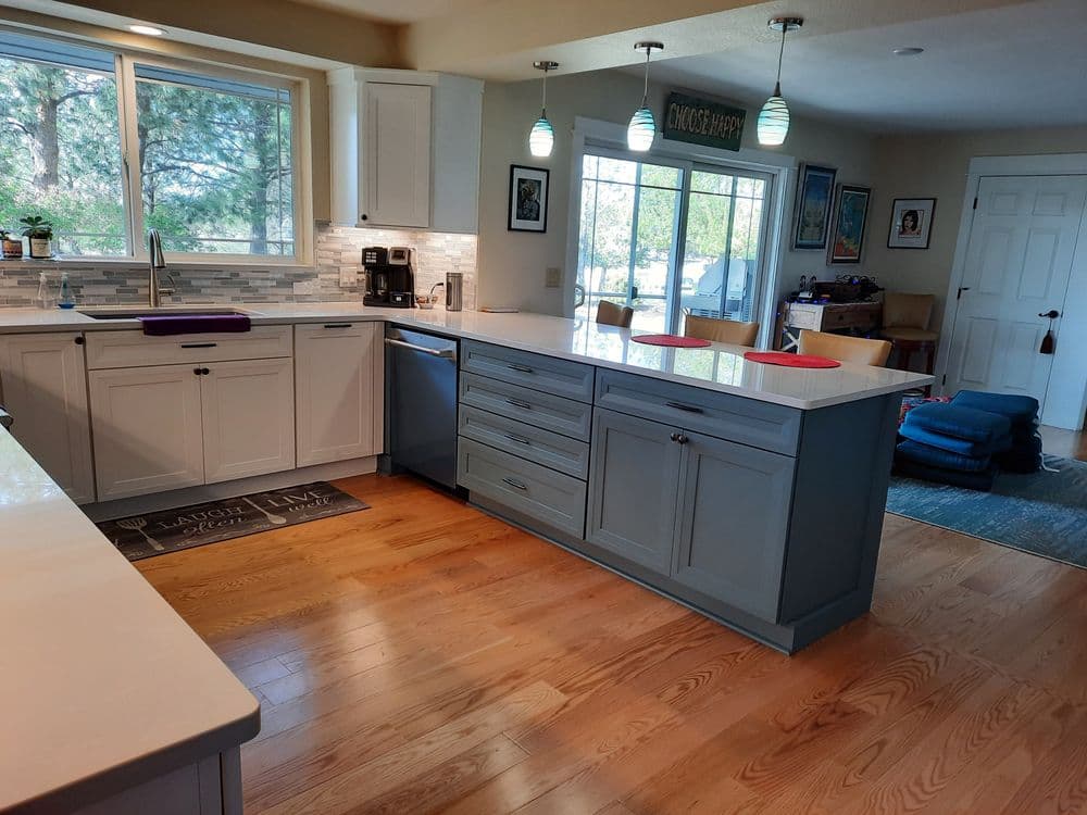 Modern kitchen with white cabinets, blue island, wooden flooring, and large windows for natural light.