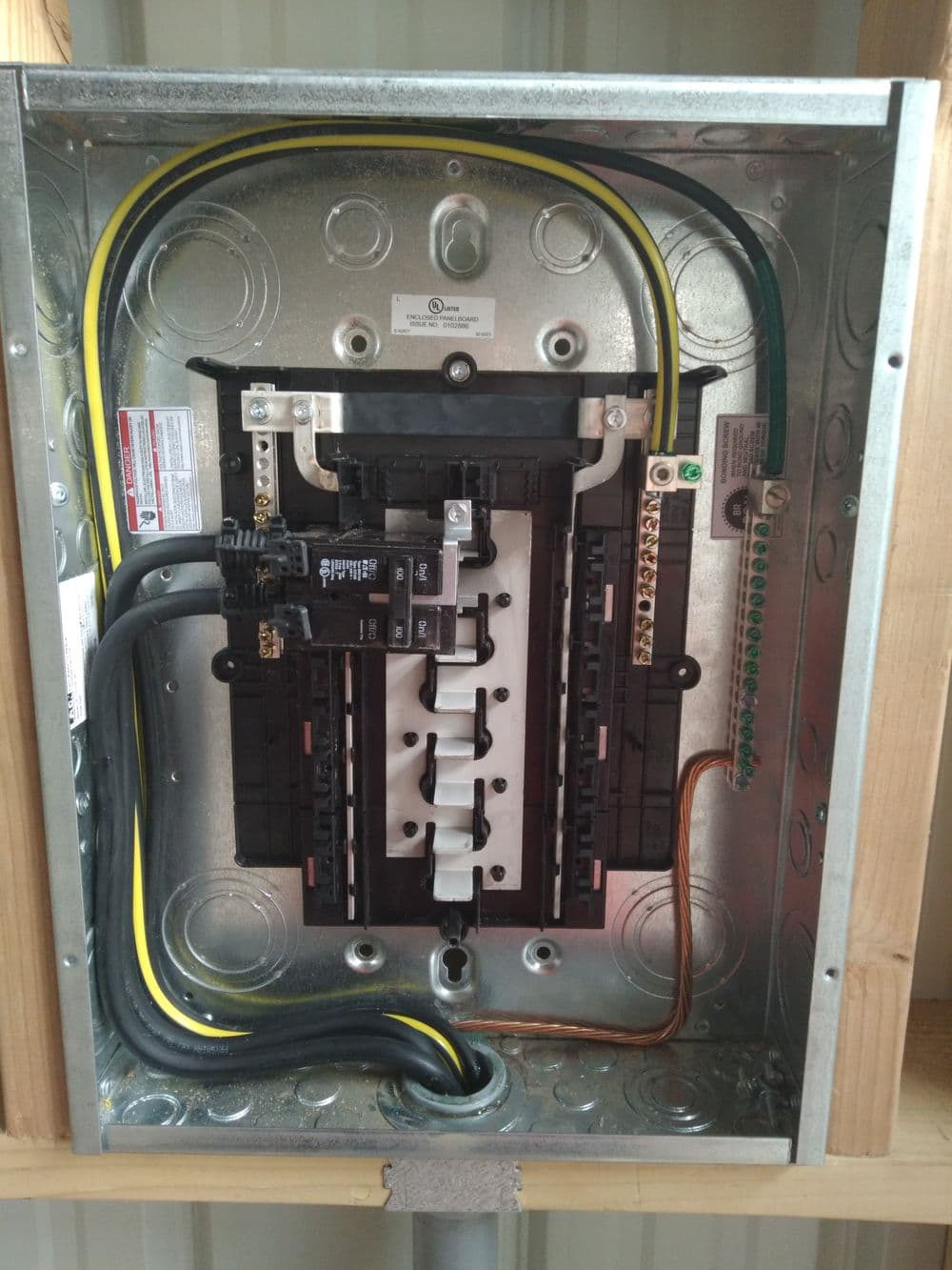Electrical panel with circuit breakers, wiring, and grounding connections in a metal enclosure.