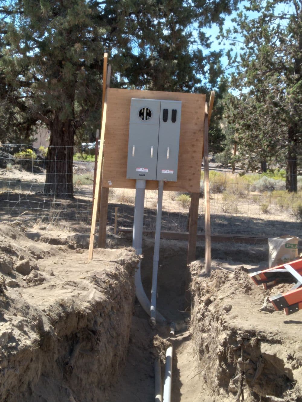 Electrical panel installation at construction site with conduit buried in trench.