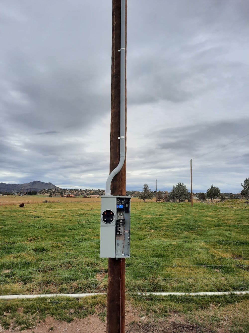 Utility pole with electrical box in an open field under a cloudy sky.