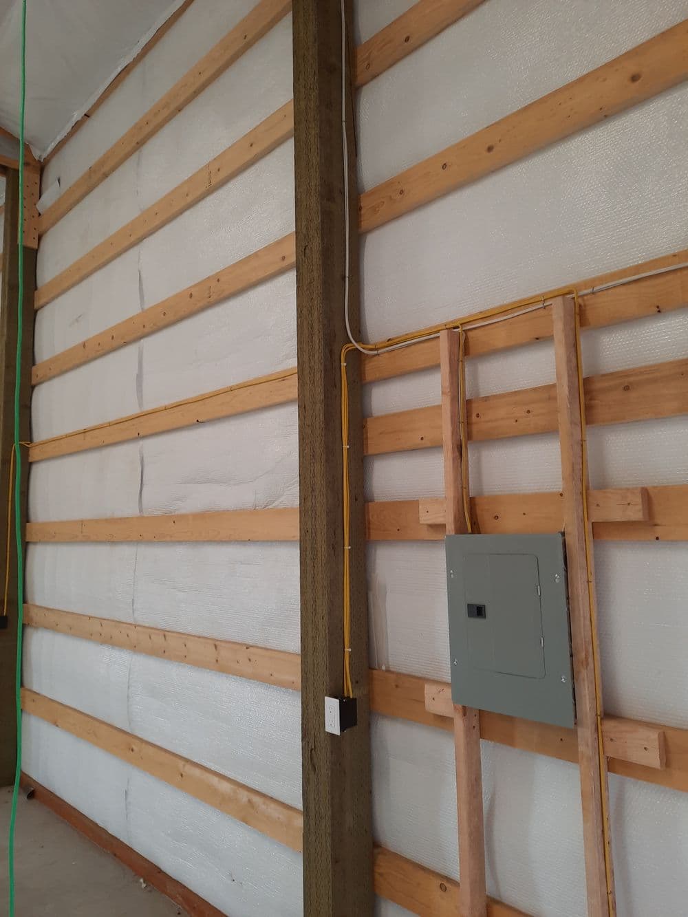 Insulated wall with wooden framing and electrical panel in a building under renovation.