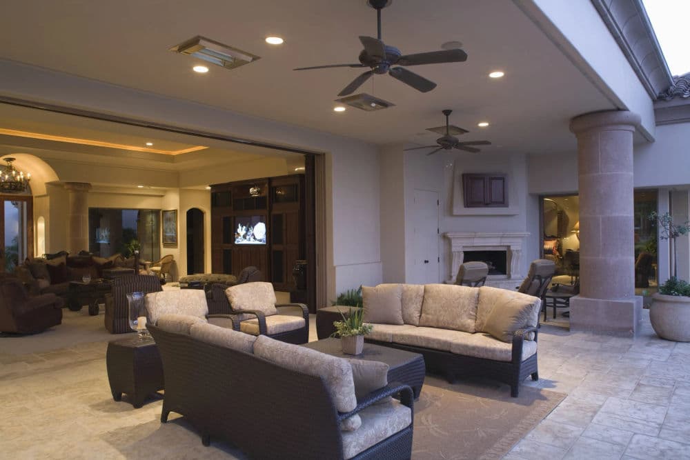 Modern outdoor patio with wicker furniture, ceiling fans, and an open view to a luxurious interior.