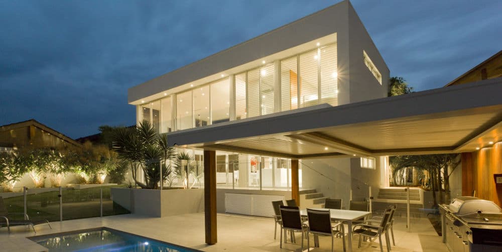 Modern two-story house with outdoor seating, pool, and evening lighting.